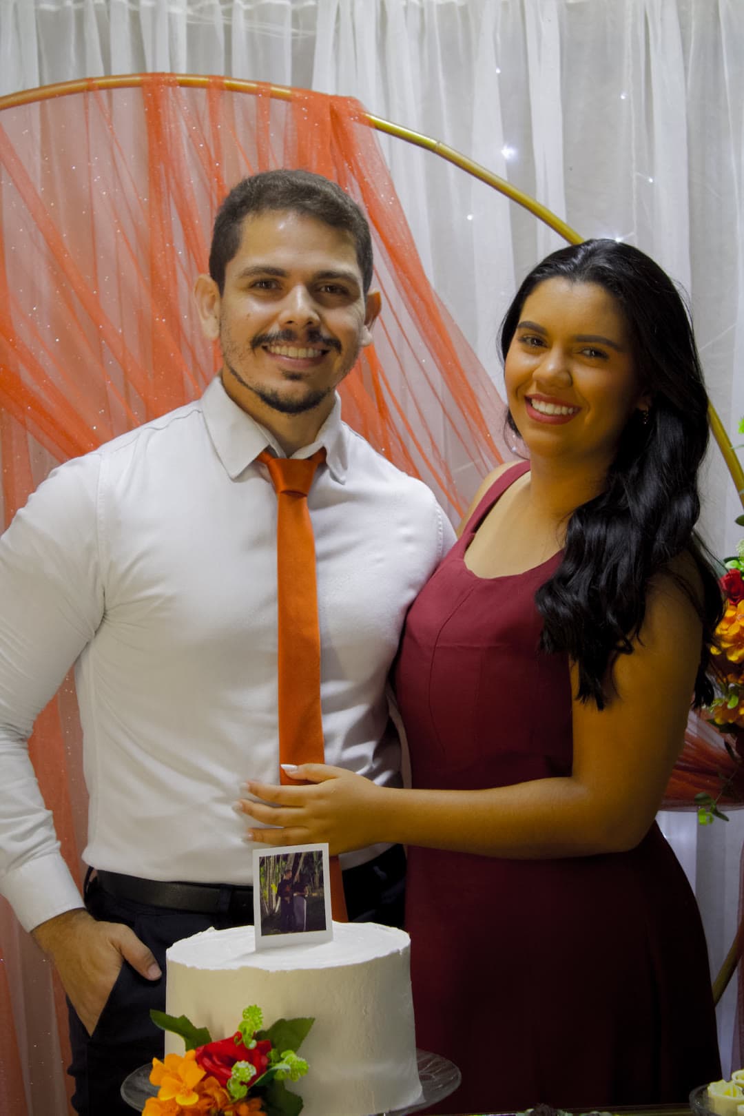 O casal sorrindo ao lado do bolo do noivado