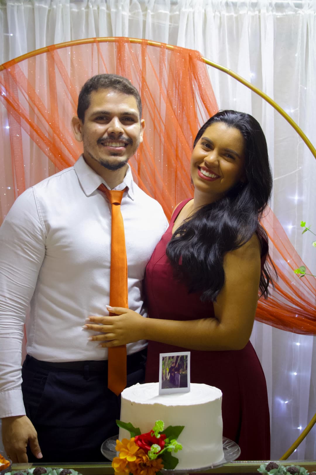 O casal com o bolo entre o tule laranja