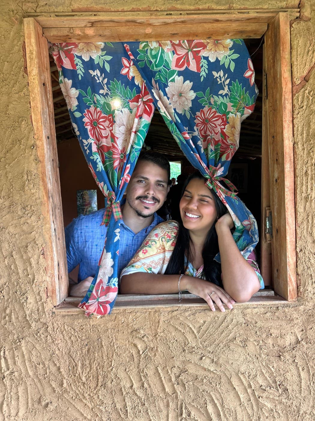 O casal sorrindo em uma janela rústica florida