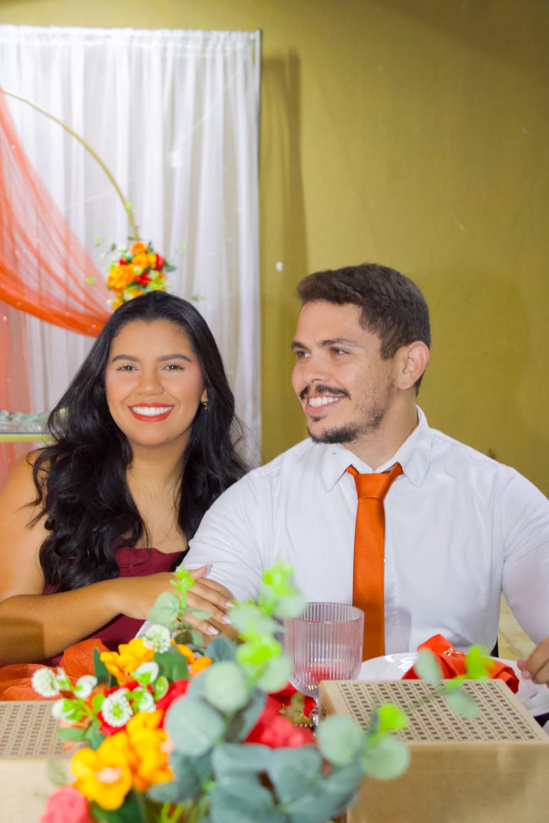 O casal sorrindo entre flores na mesa